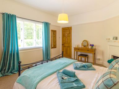 A bedroom with a bed towels dresser mirror window with curtains and wooden door at Estuary View in Warkworth