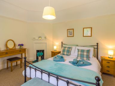 A bedroom with a double bed blue towels bedside tables dressing table and a small fireplace at Estuary View in Warkworth