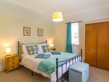 A bedroom with a metal bed frame two bedside tables with lamps a wooden wardrobe and a window with blue curtains at Estuary View in Warkworth