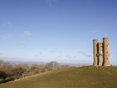 A stone tower on a grassy hill with trees and a clear sky at Beechnut Cottage in Tewkesbury