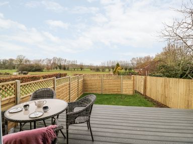 A fenced backyard with a table and chairs on a deck overlooking fields at Beechnut Cottage in Tewkesbury