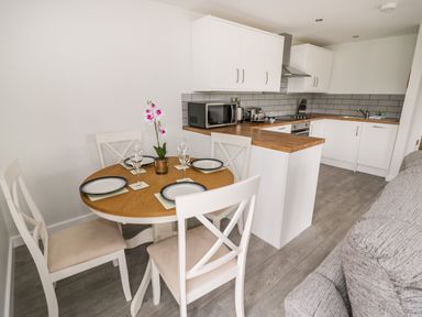 A kitchen and dining area with a round wooden table set for four and white cabinets at Beechnut Cottage in Tewkesbury