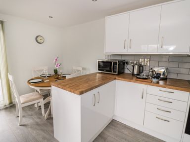 A kitchen with white cabinets wooden countertops a microwave kettle toaster and a dining table with four chairs and place settings at Beechnut Cottage in Tewkesbury
