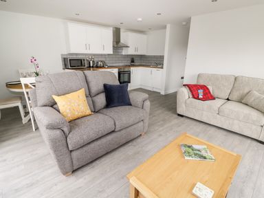 A living room with two sofas a wooden coffee table and a kitchen with white cabinets in the background at Beechnut Cottage in Tewkesbury