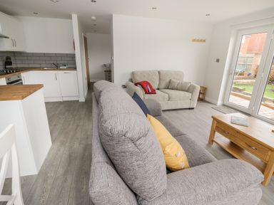 A living room with two sofas a wooden coffee table and a kitchen area at Beechnut Cottage in Tewkesbury
