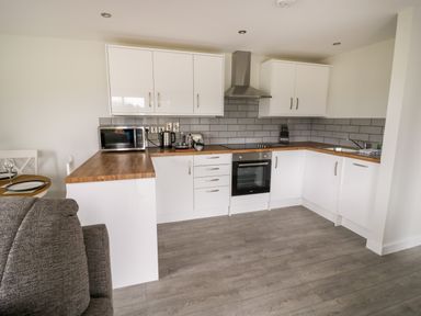 A kitchen with white cabinets wooden countertops a microwave kettle toaster and oven at Beechnut Cottage in Tewkesbury
