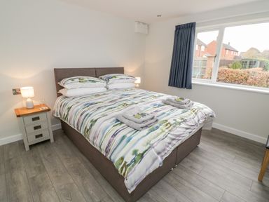 A bedroom with a double bed bedside tables lamps and a window with blue curtains at Beechnut Cottage in Tewkesbury