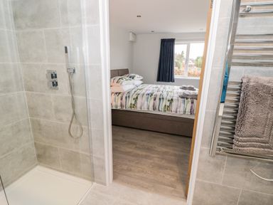 A bathroom with a walk-in shower and a heated towel rail adjacent to a bedroom with a bed and a window at Beechnut Cottage in Tewkesbury
