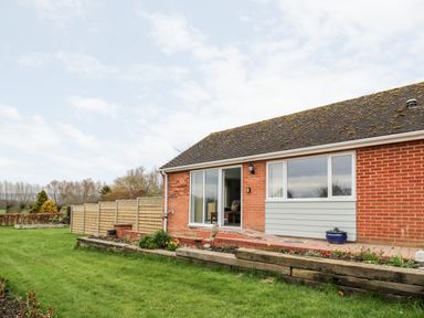 The backyard of a brick house with a lawn a wooden fence and a garden bed at Beechnut Cottage in Tewkesbury