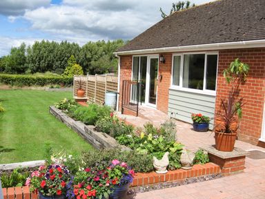Front garden with plants and flowers along a brick house with sliding doors at Beechnut Cottage in Tewkesbury