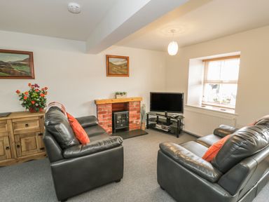 A living room with two black leather sofas a wooden cabinet a TV on a stand and a brick fireplace at Brickfield Cottage in Machynlleth