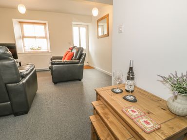 A living room with black leather sofas a bottle of wine and two wine glasses on a wooden table at Brickfield Cottage in Machynlleth