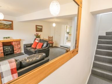A living room with black leather sofas red cushions and a fireplace reflected in a wall mirror next to carpeted stairs at Brickfield Cottage in Machynlleth
