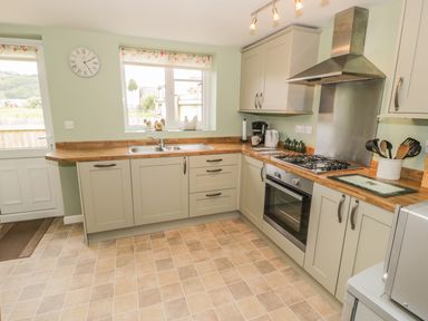 A kitchen with cabinets a stove a sink window and a door at Brickfield Cottage in Machynlleth
