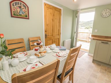A kitchen dining area with a table set for tea and door opening to a patio at Brickfield Cottage in Machynlleth