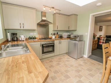 A kitchen with wooden countertops cabinets a sink coffee maker electric kettle oven microwave and refrigerator at Brickfield Cottage in Machynlleth