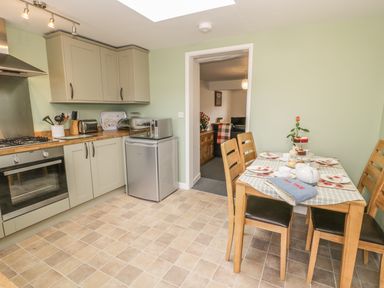 A kitchen with oven, microwave, small fridge, wooden dining table set for tea, and doorway to living room at Brickfield Cottage in Machynlleth
