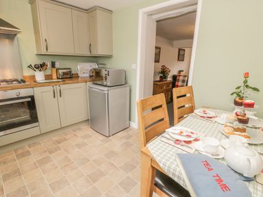 A kitchen with wooden cabinets a small refrigerator microwave and a table set for tea with cupcakes and a teapot at Brickfield Cottage in Machynlleth