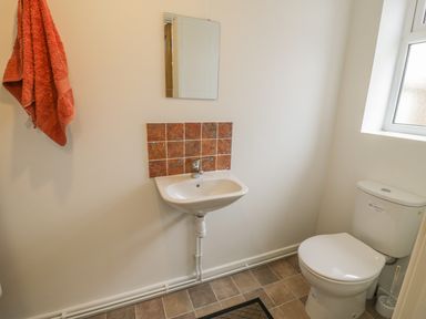 A bathroom with a toilet sink mirror and orange towel hanging on the wall at Brickfield Cottage in Machynlleth