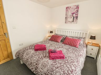 A bedroom with a double bed with patterned bedding two bedside tables with lamps and a painting above the bed at Brickfield Cottage in Machynlleth