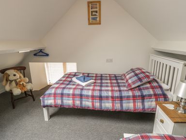 A bedroom with a bed covered in plaid bedding and a wooden chair with stuffed animals at Brickfield Cottage in Machynlleth