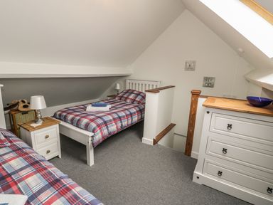 A bedroom with two single beds with plaid bedding a white dresser a nightstand with lamp and stuffed toy at Brickfield Cottage in Machynlleth
