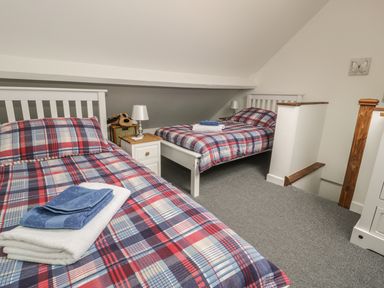 A bedroom with two single beds with plaid bedding and folded towels on the beds at Brickfield Cottage in Machynlleth