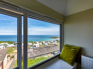 Window seat with green cushions and a view of the sea and caravans at Rocky Close in St Ives