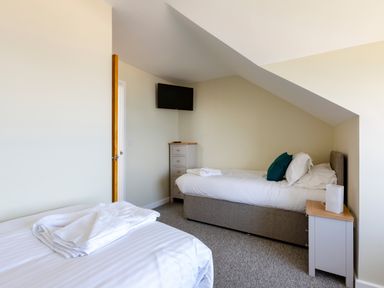 A bedroom with two single beds a chest of drawers a wall-mounted television and a bedside table at Rocky Close in St Ives