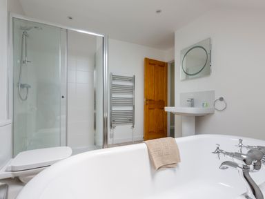 A bathroom with a bathtub a towel a shower enclosure a wooden door a towel rack a sink with a faucet and a mirror at Rocky Close in St Ives