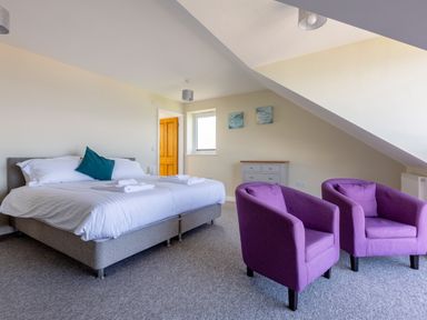 A bedroom with a bed with white bedding two purple armchairs and a chest of drawers at Rocky Close in St Ives