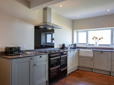 A kitchen with grey cabinets a black stove a toaster a coffee maker and a window with flowers at Rocky Close in St Ives