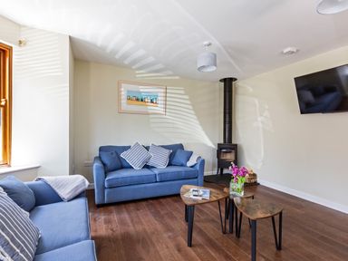 A living room with blue sofas a wood stove a wall mounted TV and nesting tables at Rocky Close in St Ives