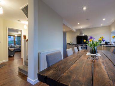 A dining room with a wooden table and chairs next to a kitchen with appliances and flowers on the table at Rocky Close in St Ives