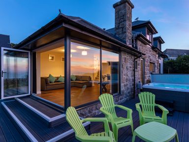 A stone house with green chairs and a hot tub on a deck outside Rocky Close in St Ives