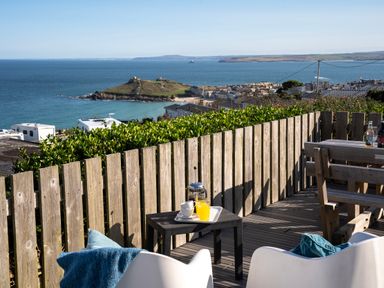 An outdoor seating area with two white chairs a small table with coffee and orange juice overlooking the sea and an island at Rocky Close in St Ives