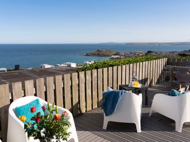 A wooden deck with white chairs and colorful cushions overlooking the sea at Rocky Close in St Ives