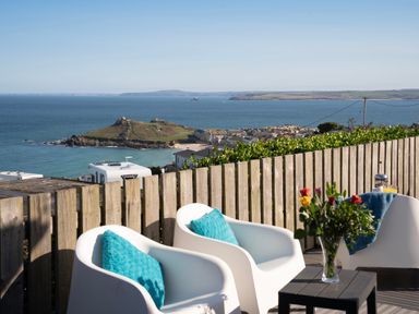 An outdoor seating area with white chairs and blue cushions overlooking the sea and a coastal town at Rocky Close in St Ives