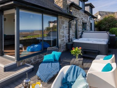 A patio area with lounge chairs, a hot tub, a table with flowers, and drinks outside a stone house at Rocky Close in St Ives