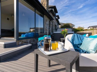 An outdoor patio with a table holding coffee and orange juice next to a white chair with blue cushions at Rocky Close in St Ives