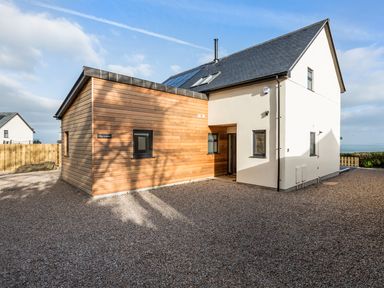 A modern house with wood paneling and white walls on a gravel driveway at Chy Lowen in St Ives