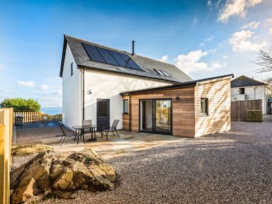 A house with solar panels on the roof patio with chairs and table and gravel driveway at Chy Lowen in St Ives