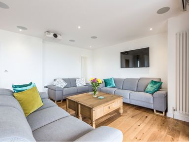 A living room with three gray sofas a wooden coffee table with flowers and a mounted television at Chy Lowen in St Ives