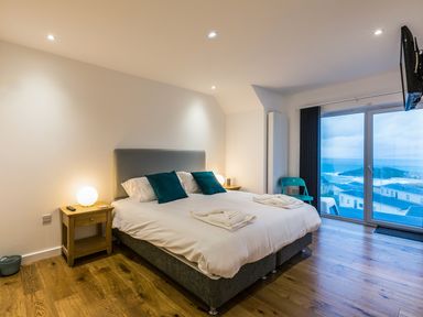 A bedroom with a double bed bedside tables and a large window with a sea view at Chy Lowen in St Ives