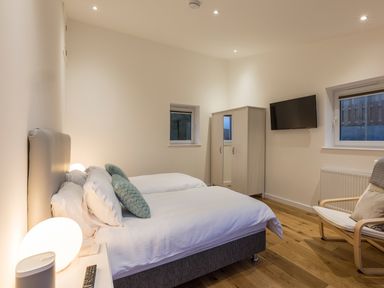 A bedroom with two beds a wardrobe a wall-mounted tv and a chair at Chy Lowen in St Ives