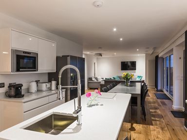 A kitchen and dining area with a sink, chairs, flowers on tables and a television at Chy Lowen in St Ives
