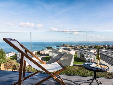 A deck chair and table with wine glasses overlooking a coastal holiday park at Chy Lowen in St Ives