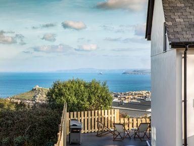 An outdoor deck with wooden chairs and a grill overlooking a coastal town and the sea at Chy Lowen in St Ives