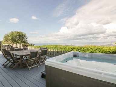 An outdoor deck with a dining table and chairs a hot tub and a view of the sea at Chy Lowen in St Ives