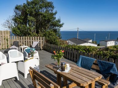 A wooden patio with chairs tables flowers and a coffee pot overlooking the sea at Chy Lowen in St Ives